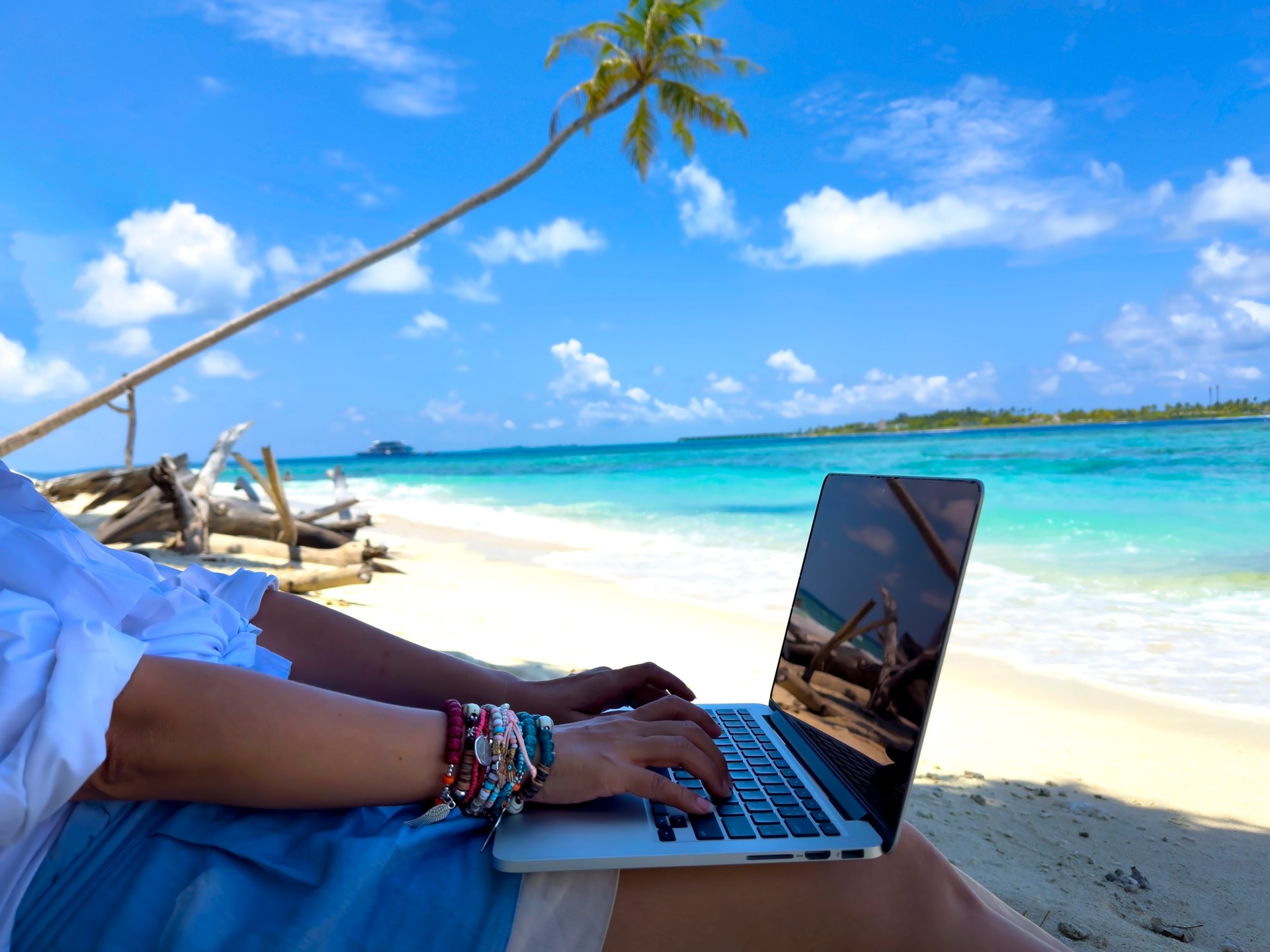 Nomad digital with laptop and running remotely with bright scenic view near poolside on the beach in summer time